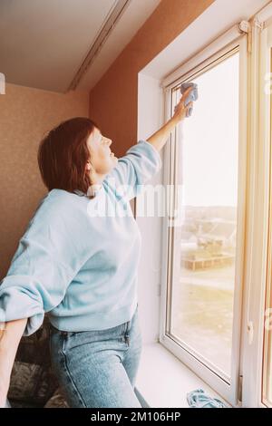 Glücklich Schüchtern Positive Reife Frau Reinigung Fenster. Konzept Für Aktive Senioren. Ältere Frau Reinigung Apartment. Hausfrau. Kaukasische Frau Im Mittleren Alter Stockfoto