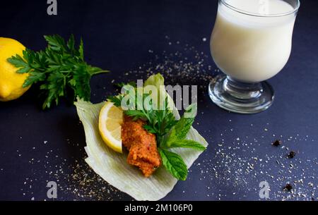 Präsentation roher Fleischbällchen auf Salat und Zitrone auf schwarzem Hintergrund, Nahaufnahme türkischer „Cigkofte“. Stockfoto