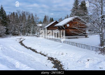 Holzhaus, Ferienhaus am Waldrand auf dem Hügel im ersten Schnee, verschneite Landschaft mit weißen Wiesen und Bäumen. Advent und Weihnachtszeit Ferien Stockfoto