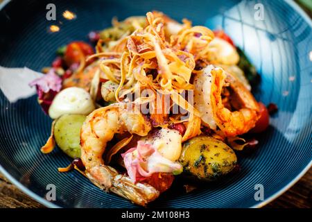 Warmer Salat mit argentinischen Königsgarnelen. Mandelkartoffel, Mini-Romana-Salat, Karotten, Kirschtomaten, Pesto, Schwarze Wurzelchips, karamellisierte Walnüsse, Rüben Stockfoto