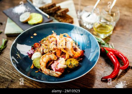 Warmer Salat mit argentinischen Königsgarnelen. Mandelkartoffel, Mini-Romana-Salat, Karotten, Kirschtomaten, Pesto, Schwarze Wurzelchips, karamellisierte Walnüsse, Rüben Stockfoto