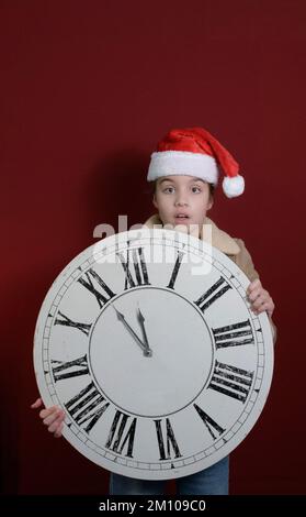 Fünf Minuten bis zum neuen Jahr. Ein Mädchen mit einer großen, alten Wanduhr in der Hand. Er trägt einen Weihnachtsmannmütze, einen begeisterten Blick in die Kamera. Platz für Text Stockfoto