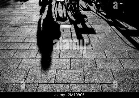 Lange Schatten von Stühlen, Tischen und Figuren in Schwarz und Weiß. Dramatische Hintergrundbeleuchtung mit Schatten, die direkt auf die Kamera zugehen. Schattenkonzept Stockfoto