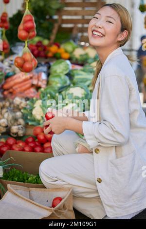 Asiatische Frau, Supermarkt- und Lebensmitteleinkäufe und Tomaten, Kunde und Einzelhandel, frische Gemüseprodukte und Lebensmittel im Geschäft kaufen. Junge, glückliche Frau Stockfoto