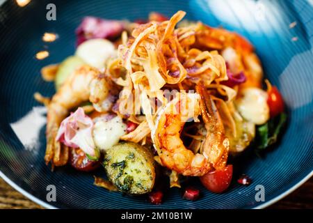 Warmer Salat mit argentinischen Königsgarnelen. Mandelkartoffel, Mini-Romana-Salat, Karotten, Kirschtomaten, Pesto, Schwarze Wurzelchips, karamellisierte Walnüsse, Rüben Stockfoto