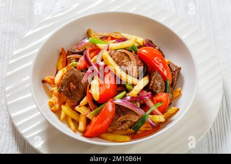 Lomo Saltado, peruanisches Gericht mit gebratenen Scheiben Rinderfilet, Zwiebeln, gelben peruanischen Chilis und Tomaten gemischt mit Pommes frites in einer weißen Schüssel Stockfoto