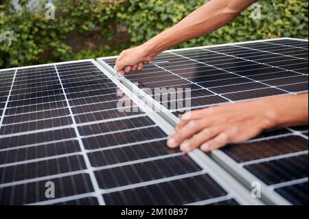 Ein Mann, der Photovoltaik-Solarmodule auf dem Dach des Hauses montiert. Nahaufnahme eines Elektrikers, der ein Solarpaneelsystem mithilfe eines Inbusschlüssels installiert. Konzept alternativer und erneuerbarer Energien. Stockfoto