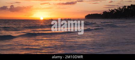 Atlantikküste bei Sonnenaufgang, Bavaro Strand, Dominikanische Republik. Panorama Küstenlandschaft mit aufstrebender Sonne, Palmen Silhouetten in Farbe Stockfoto