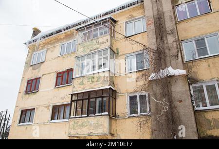 Mehrere, schmelzende Eiszapfen hängen am Dachrand, im Frühling oder Winter. Wand eines alten Backsteinhauses mit Fenstern. Große Eiszapfen in glatten, schönen Reihen. Bewölkter Wintertag, weiches Licht. Stockfoto