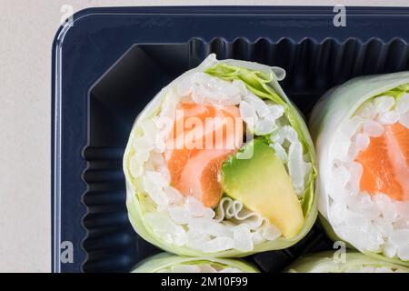 Lachs- und Avocado-Maki mit Reislaken in einer Plastikschale zum Mitnehmen. Draufsicht. Makroaufnahme Stockfoto