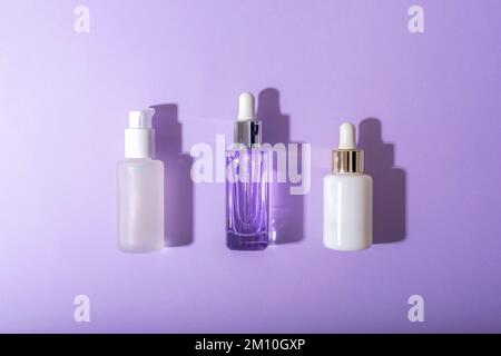 Kosmetikserumflaschen auf violettem Hintergrund mit harten Schatten. Draufsicht, flaches Lay, Modell. Stockfoto