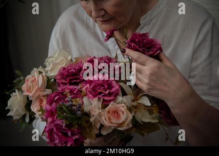 Ein Strauß weißer Rosen und burgunderfarbenen Nelken in der Hand einer Frau in einem weißen Hemd Stockfoto