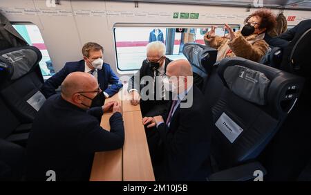 09. Dezember 2022, Baden-Württemberg, Ulm: Winfried Hermann (von links, Bündnis 90/die Grünen), Verkehrsminister von Baden-Württemberg, Vorstandsvorsitzender der Deutschen Bahn AG, Richard Lutz, Winfried Kretschmann (Bündnis 90/die Grünen), Verkehrsminister von Baden-Württemberg und Michael Theurer, Bundeskommissar für Verkehr (FDP) Setzen Sie sich während der Sonderreise in den Spezialzug, um die Eröffnung der neuen Eisenbahnlinie Wendlingen-Ulm zu feiern. Rechts ist Gerlinde Kretschmann, die Frau des Ministerpräsidenten. Ein EISZUG mit eingeladenen Gästen ist die Reise Stockfoto