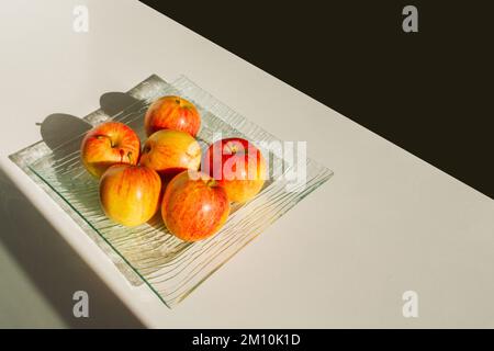 Ein Äpfelset auf einem durchsichtigen Gericht. Äpfel sind gelb-rot. Hartes Licht. Stockfoto