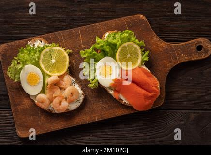 Die Toasts mit gekochten Eiern, Salat, Zitronenschleim, Garnelen und geräuchertem Lachs. Stockfoto