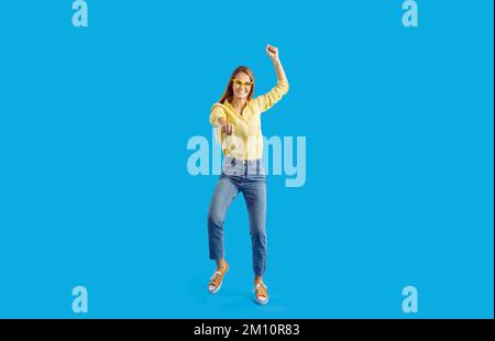 Fröhliche junge Frau tanzt euphorisch und feiert Erfolg auf blauem Hintergrund. Stockfoto
