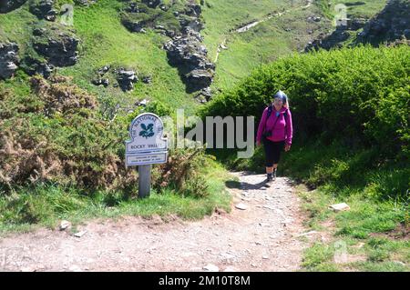 Woman Climbing Stufen von Wooden Foot Bridge über den Fluss Trevillett im Rocky Valley auf dem South West Coastal Path, Cornwall, England, Großbritannien. Stockfoto