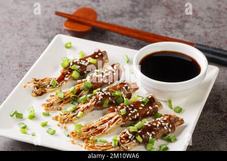 Köstliches gebratenes Rinderbrötchen mit Enoki-Pilzen mit Teriyaki-Sauce, grünen Zwiebeln und Sesam aus nächster Nähe auf einem Teller auf dem Tisch. Horizontal Stockfoto