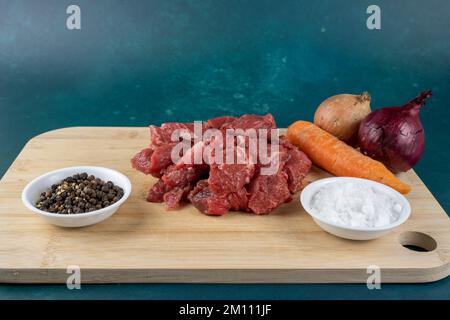 Rohes Rindfleisch, das in kleine Stücke geschnitten und mit Salz und Pfeffer auf einem Bambusschneidbrett gewürzt werden kann Stockfoto