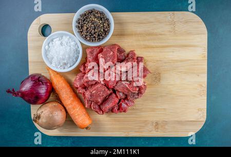 Grundlegende Rohstoffe von rohem gewürfeltem Rindfleisch, Karotten und Zwiebeln mit Gewürzen auf einem Bambusschneidbrett Stockfoto