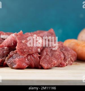 Nahaufnahme von etwas rohem Rindfleisch, das in kleine Würfel geschnitten wurde, in einem Bambusschneidbrett Stockfoto