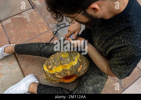 Ein junger Mann mit einem Bohrer oder dremel, der einen Kürbis zu halloween bohrt Stockfoto