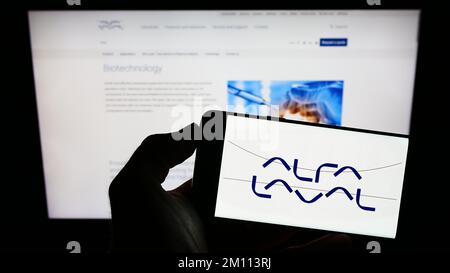 Person, die ein Mobiltelefon mit dem Logo des schwedischen Unternehmens Alfa Laval ab auf dem Bildschirm vor der Unternehmenswebseite hält. Konzentrieren Sie sich auf das Display des Telefons. Stockfoto