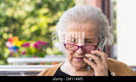Alte Frau mit Brille, die am Telefon spricht. Eine alte Frau hört schlechte Nachrichten am Telefon und macht einen traurigen Gesichtseindruck. Stockfoto
