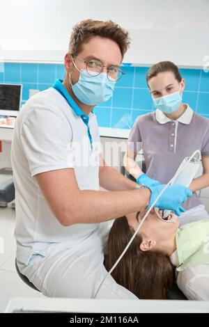 Stomatologe mit diagnostischem Gerät zur Untersuchung der Mundhöhle junger Frauen Stockfoto
