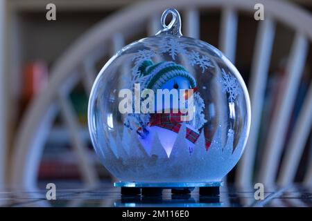 Ein beleuchteter Schneemann in einem Globus sitzt zu Weihnachten auf einem Tisch Stockfoto