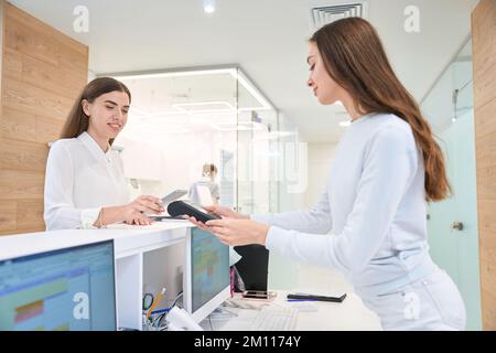 Lächelnde Frau, die mit Smartphone an der Rezeption der Klinik bezahlt Stockfoto