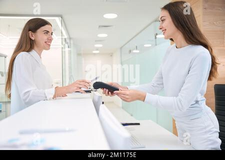 Zufriedener Kunde, der mit dem Mobilgerät an der Rezeption bezahlt Stockfoto