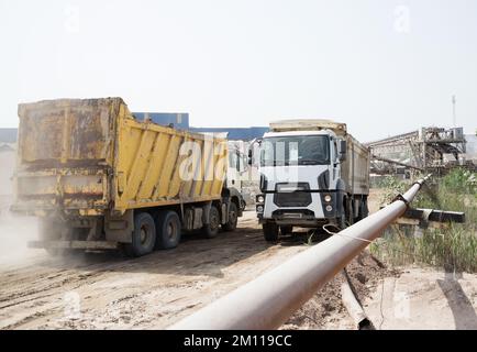 Zwei Kipplaster fahren auf sandiger Straße in entgegengesetzter Richtung. Staub, Dreck, Erdarbeiten. Transport verschiedener Materialien auf der Baustelle. Ope Stockfoto