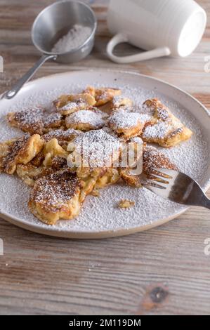 hausgemachtes kaiserschmarrn mit Puderzucker auf einer weißen Platte auf hellem Holzhintergrund Stockfoto