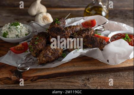 Mediterrane Hackfleischspieße mit Dippsauce auf rustikalem Holztisch Stockfoto