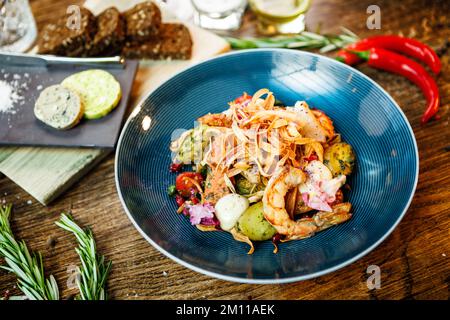 Warmer Salat mit argentinischen Königsgarnelen. Mandelkartoffel, Mini-Romana-Salat, Karotten, Kirschtomaten, Pesto, Schwarze Wurzelchips, karamellisierte Walnüsse, Rüben Stockfoto