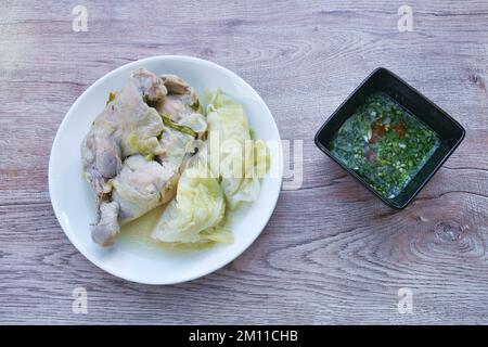 Gedünstetes, würziges Hähnchen an Oberschenkel und Bein mit Kohl in Kräutersuppe auf Teller, mit würziger Chilisauce Stockfoto