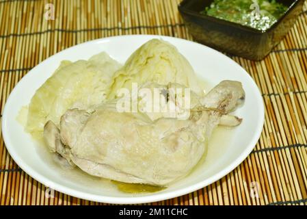 Gedünstetes, würziges Hähnchen an Oberschenkel und Bein mit Kohl in Kräutersuppe auf Teller, mit würziger Chilisauce Stockfoto