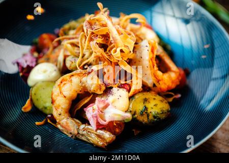 Warmer Salat mit argentinischen Königsgarnelen. Mandelkartoffel, Mini-Romana-Salat, Karotten, Kirschtomaten, Pesto, Schwarze Wurzelchips, karamellisierte Walnüsse, Rüben Stockfoto