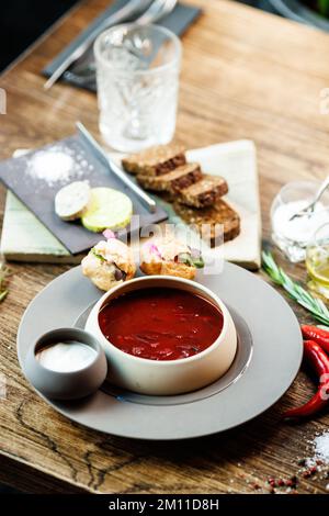 Rote-Bete-Suppe Borscht mit Fleisch und Sauerrahm in einer Schüssel. Köstliche, gesunde ukrainische traditionelle Küche serviert zum Mittagessen auf einem Tisch in modernem Stil Stockfoto
