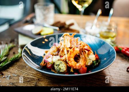 Warmer Salat mit argentinischen Königsgarnelen. Mandelkartoffel, Mini-Romana-Salat, Karotten, Kirschtomaten, Pesto, Schwarze Wurzelchips, karamellisierte Walnüsse, Rüben Stockfoto