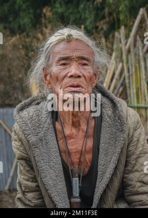 Ziro, Arunachal Pradesh, Indien - 02 19 2013 : Portrait des alten Apatani-Stammesmanns mit traditionellem Kinn-Tattoo und frontalem Haarbrötchen, der draußen sitzt Stockfoto