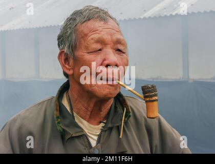 Raga, Arunachal Pradesh, Indien - 02 25 2009 : Porträt des alten Nyishi-Stammes, der traditionelle Bambuspfeife raucht, im Freien auf nebligen Hintergrund Stockfoto