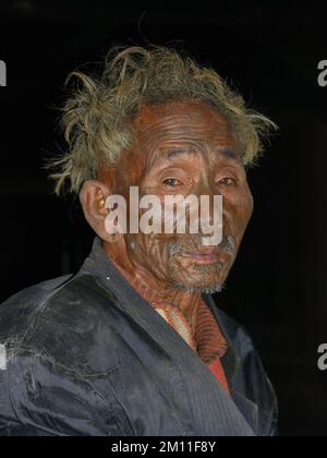 Mon District, Nagaland, Indien - 03 02 2009 : Portrait des alten Naga Konyak-Stammesführers mit traditioneller Tätowierung im Gesicht auf schwarzem Hintergrund Stockfoto