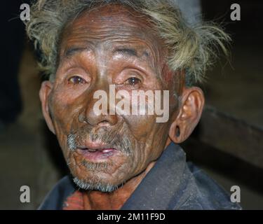 Mon District, Nagaland, Indien - 03 02 2009 : Portrait des alten Naga Konyak-Stammesführers mit traditioneller Tätowierung im Gesicht auf dunklem Hintergrund Stockfoto