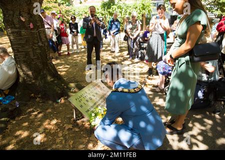 Der Bürgermeister von Camden, Cllr Nasim Ali, legt in der Nähe des Kirschbaums, der zum Gedenken an die Opfer von Hiroshima während eines Ereignisses in London gepflanzt wurde, Blumengewächse ab. Stockfoto