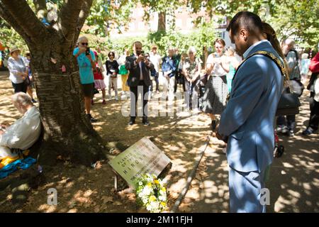 Bürgermeister von Camden, Cllr Nasim Ali, beobachtet eine Stille in der Nähe des Kirschbaums, der zum Gedenken an die Opfer von Hiroshima während einer Veranstaltung in London gepflanzt wurde. Stockfoto