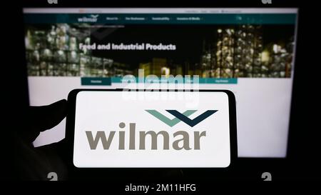 Person, die ein Smartphone mit dem Logo des singapurischen Unternehmens Wilmar International Limited auf dem Bildschirm vor der Website hält. Konzentrieren Sie sich auf das Display des Telefons. Stockfoto