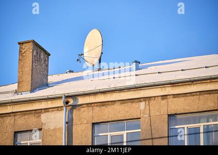 Alte Satellitenschüssel auf dem Dach mit Kamin am blauen Himmel Stockfoto