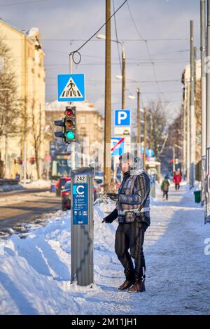 Riga, Lettland - 8. Dezember 2022: Mitarbeiter, der im Winter den Parkkartenautomaten auf der Straße überprüft Stockfoto